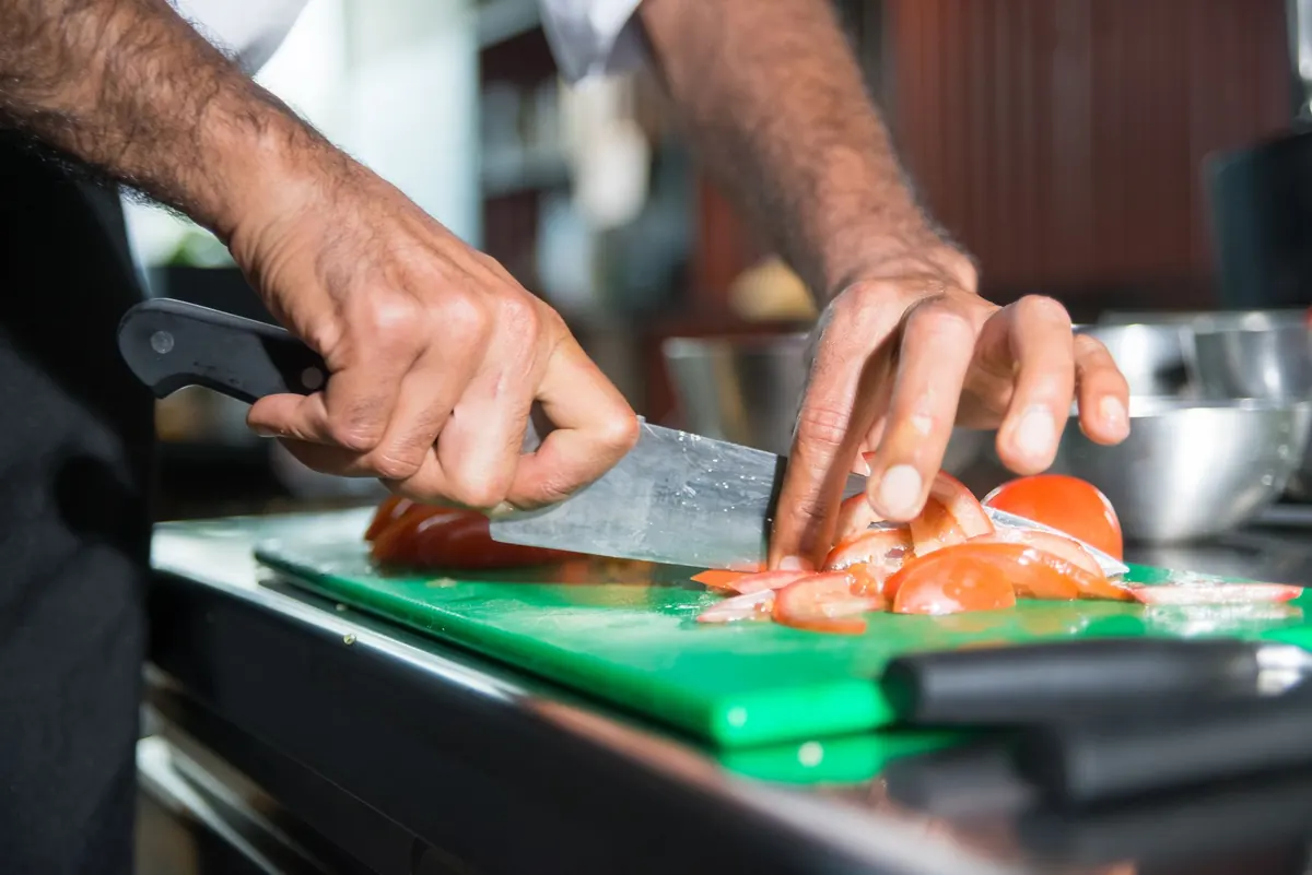 Chef slicing fresh tomatoes on a colour-coded chopping board in a restaurant kitchen