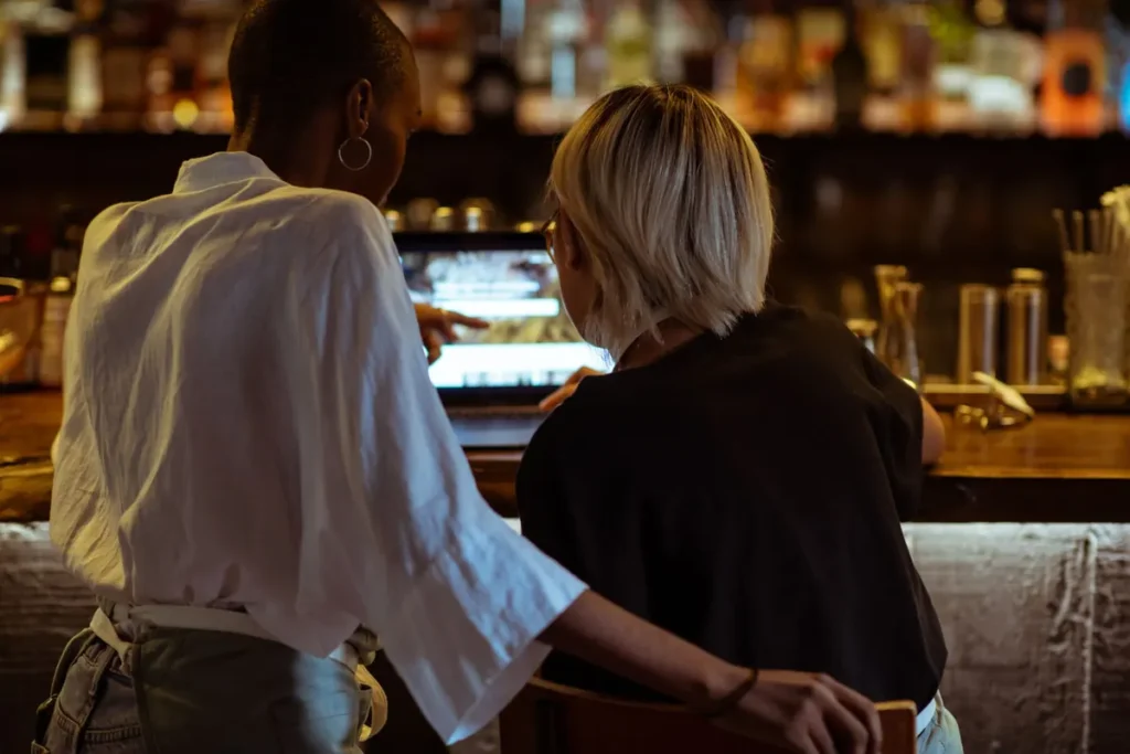 Two restaurant staff reviewing work on a laptop at the bar before service