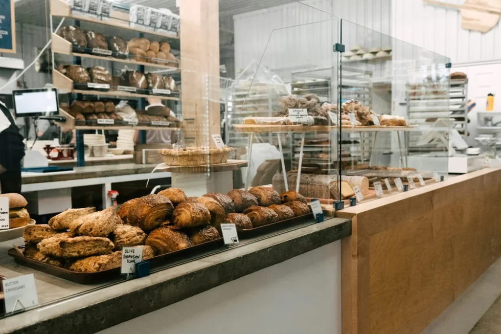 Bakery pastry and bread display case with price tags and a POS screen at the counter