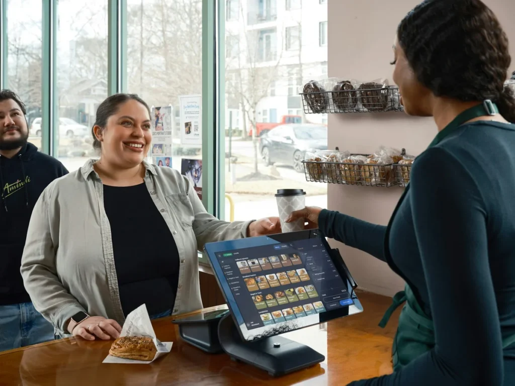 Barista handing a coffee to a customer over a cafe POS tablet at the counter